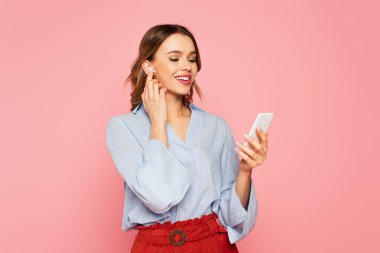 Kulaklıklı güzel bir kadın pembe üzerine izole edilmiş akıllı telefon kullanıyor. 