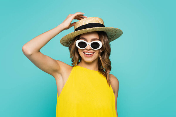 Cheerful woman in sun hat and sunglasses isolated on blue 