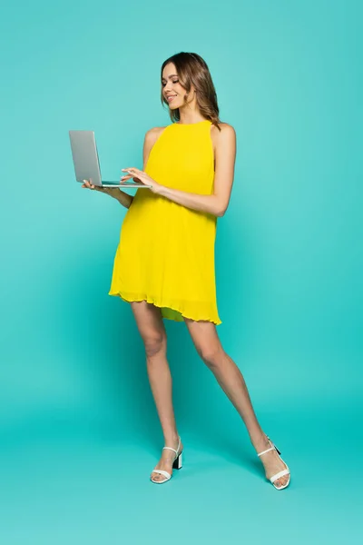 Młoda Kobieta Żółtej Sukience Pomocą Laptopa Niebieskim Tle — Zdjęcie stockowe