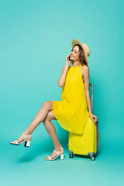陽気女性で太陽帽子Talkingオンスマートフォン上のスーツケース上の青の背景 — ストック写真