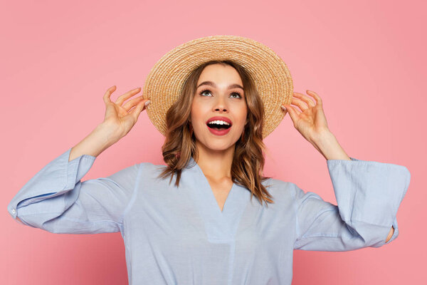 Astonished woman in sun hat looking up isolated on pink 