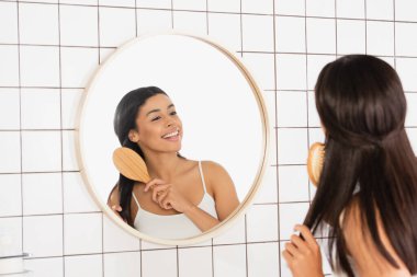 Genç Afrikalı Amerikalı kadın banyoda aynanın yanında saç tarıyor.