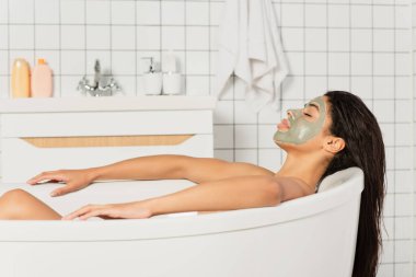 Yüzünde çamur maskesi olan barışçıl Afro-Amerikalı kadın banyo yapıyor.