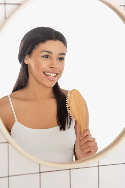 在浴室的镜子前拿着梳子的年轻非洲女人微笑着 — 图库照片
