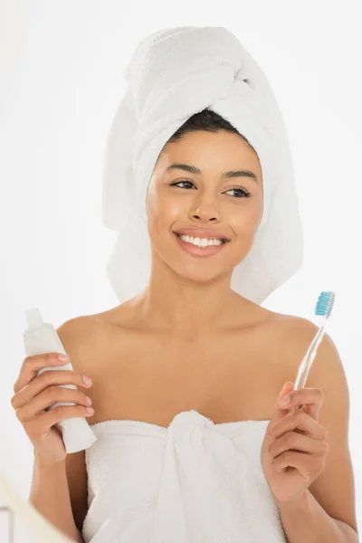 在浴室里拿着牙刷和牙膏 裹在毛巾里的积极的非洲裔美国妇女 — 图库照片