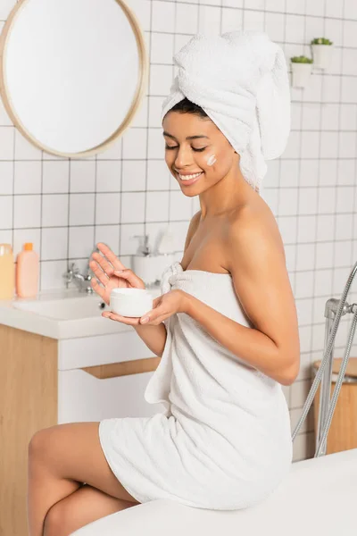 Sonriente Joven Afroamericana Mujer Sentada Baño Sosteniendo Frasco Con Crema — Foto de Stock