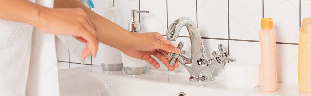 cropped view of female young hands touching faucet before washing in bathroom, banner