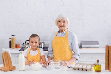Grandmother and smiling kid looking at camera near ingredients and digital tablet  clipart