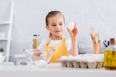Gülümseyen çocuk önplanda şeker ve yağ yanında yumurtayı tutuyor 