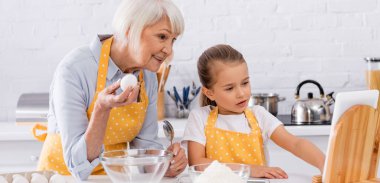 Elinde kaşıkla yumurta tutan gülümseyen yaşlı kadın dijital tablet ve pankart kullanıyor. 
