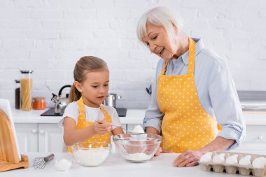 Gülümseyen büyükannenin yanına un döken çocuk, dijital tablet ve malzemeler. 