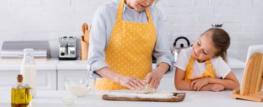 Gülümseyen torunun yanında hamuru buruşturan yaşlı kadın, dijital tablet ve mutfak malzemeleri, afiş.