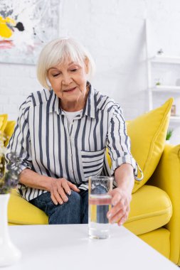 Gülümseyen yaşlı kadın bulanık bir bardak su alıyor. 