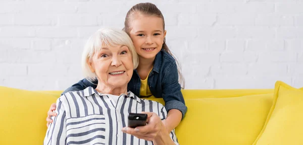 Leende Unge Kramar Mormor Med Fjärrkontroll Hemma Banner — Stockfoto