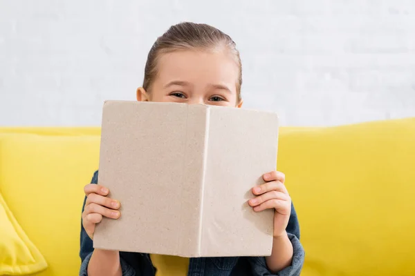 Criança Cobrindo Rosto Com Livro Sofá Embaçado — Fotografia de Stock