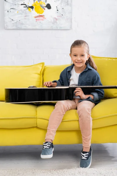 Criança Positiva Sorrindo Para Câmera Perto Guitarra Acústica Sofá — Fotografia de Stock