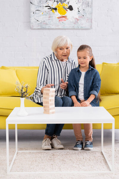 Старшая женщина говорит и указывает на блоки древесины игры рядом с ребенком 