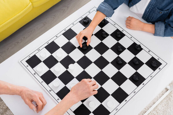 Cropped view of elderly woman and child playing checkers at home 