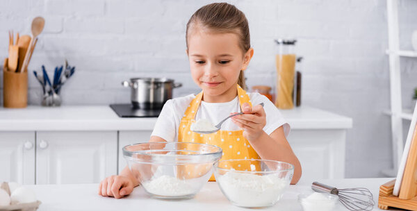 Smiling girl in apron pouring flour near eggs and digital tablet in kitchen, banner 
