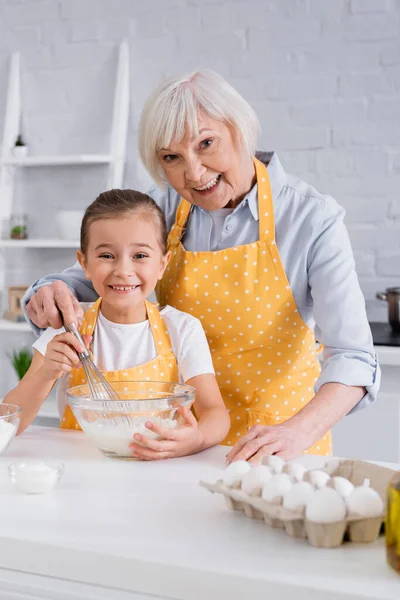 Ευτυχισμένο Παιδί Και Γιαγιά Κοιτάζοντας Κάμερα Ενώ Μαγείρεμα Στην Κουζίνα — Φωτογραφία Αρχείου
