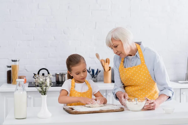 奶奶在厨房里拿着面粉 小孩在牛奶边做面团 — 图库照片