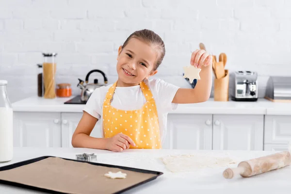 快乐的女孩拿着面团靠近烤盘和饼干切割机 — 图库照片
