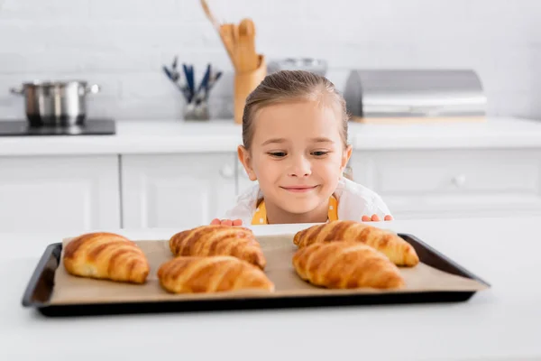 Happy Kid Regardant Des Croissants Flous Sur Une Plaque Pâtisserie — Photo