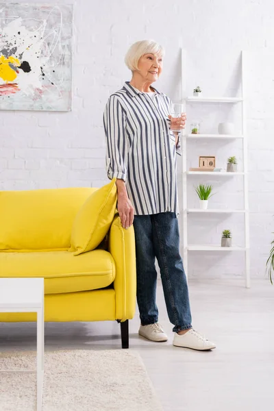 Šťastná Starší Žena Sklenicí Vody Stojící Obývacím Pokoji — Stock fotografie
