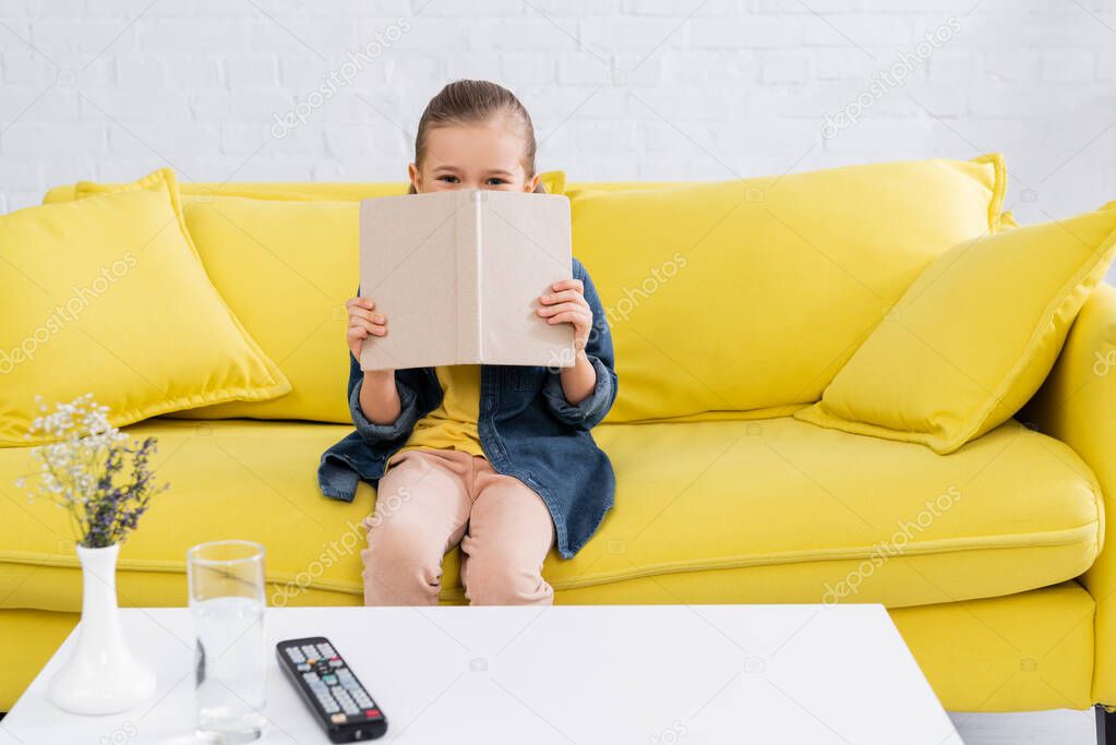 Girl holding book near face on couch at home 