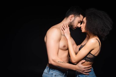Siyah üzerine izole edilmiş seksi Afro-Amerikan kadını kucaklayan dövmeli adamın yan görüntüsü. 