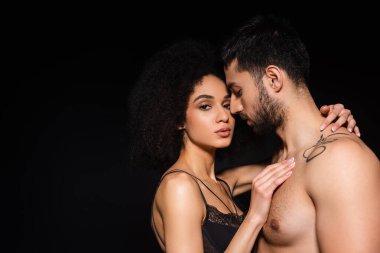 Seksi Afro-Amerikalı kadın kameraya bakarken siyahi bir adamı kucaklıyor. 