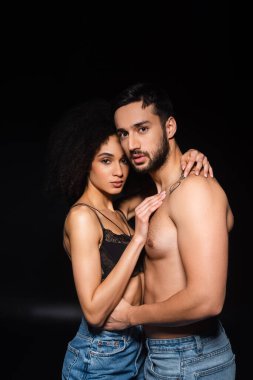 Siyah arka planda sarılıp kameraya bakan ırklar arası seksi bir çift. 