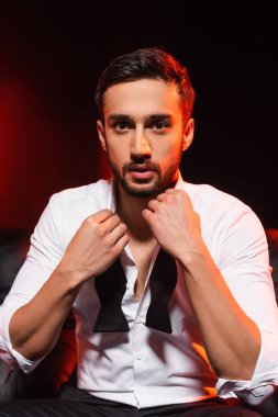 Siyah arka planda papyon tutan sakallı genç bir adam.