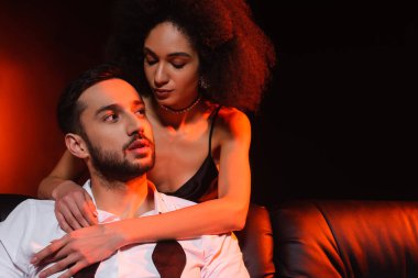 Siyah arka planda erkek arkadaşına sarılan Afrikalı Amerikalı bir kadın.