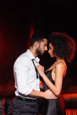 Siyah arka planda siyah ışıklandırmalı Afro-Amerikan kız arkadaşına sarılan adamın yan görüntüsü