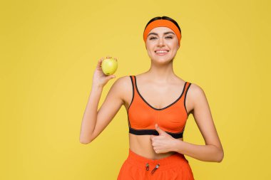 Mutlu sporcu kadın yeşil elma tutuyor ve sarı renkte başparmağını kaldırıyor.