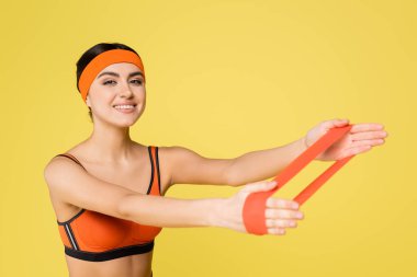 Sarı bantlı direniş bandıyla egzersiz yaparken kameraya gülümseyen neşeli sporcu kadın