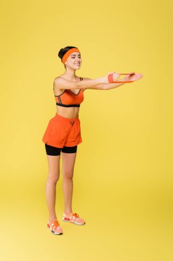 full length view of happy sportswoman training with elastics isolated on yellow clipart