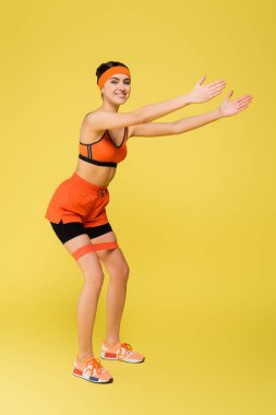 Sarı lastikle egzersiz yaparken kameraya bakan neşeli sporcu kadın.
