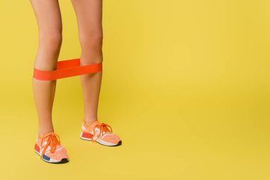 Sarı arka planda bacaklarında direnç bandı olan sporcu kadın eğitiminin kırpılmış görüntüsü