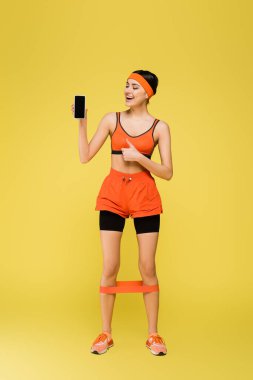 Cep telefonlu mutlu sporcu kadın sarı renkte başparmağını gösteriyor.