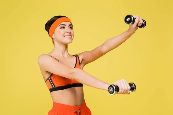 Glimlachende Sportvrouw Oranje Sportkleding Training Met Halters Geïsoleerd Geel — Stockfoto