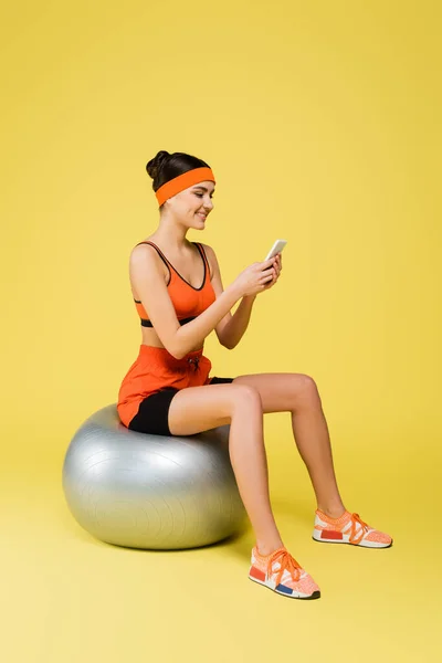 Sportive Woman Sitting Fitness Ball Messaging Mobile Phone Yellow Background — Foto de Stock