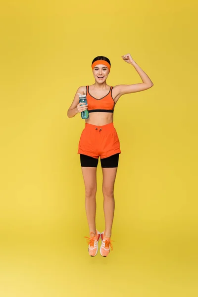 Cheerful Sportswoman Sports Bottle Jumping Showing Win Gesture Isolated Yellow — Stock Photo, Image