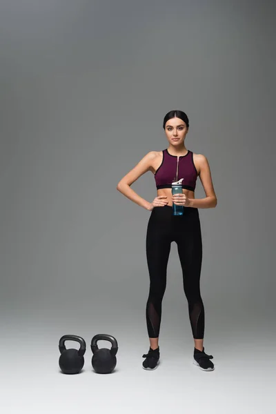 Confident Woman Sports Bottle Standing Kettlebells Grey Background — Foto de Stock