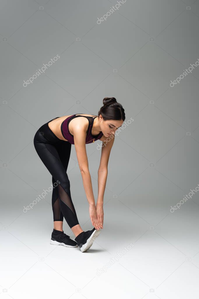 young sportswoman doing forward bend exercise on grey background