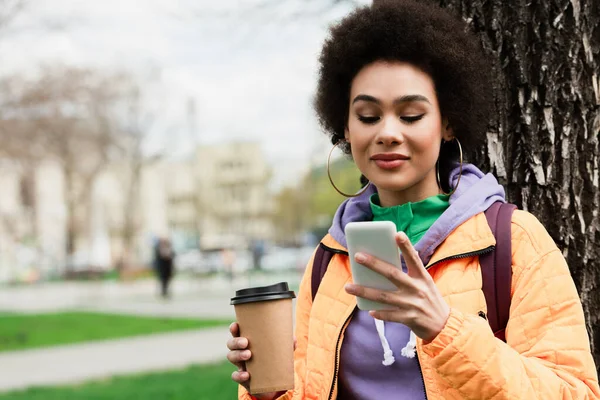 Glimlachende Afrikaans Amerikaanse Vrouw Met Mobiele Telefoon Houden Afhaaldrankje Buiten — Stockfoto