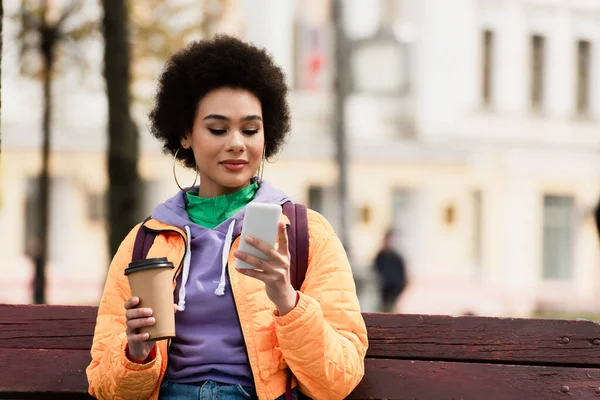 Csinos Afro Amerikai Kabátban Mobiltelefonnal Papírpohárral Padon — Stock Fotó