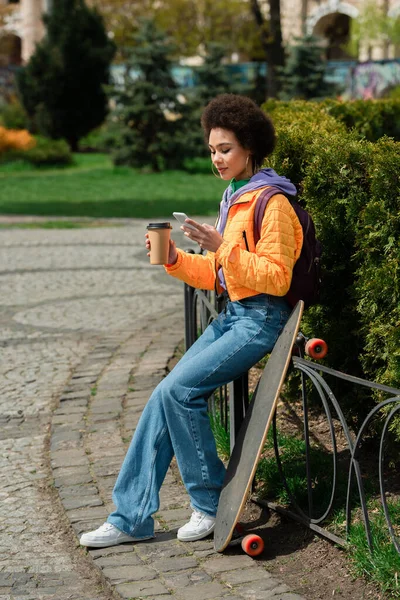 Afroamerykanka Kubkiem Wynos Pomocą Telefonu Komórkowego Pobliżu Longboard Ulicy Miejskiej — Zdjęcie stockowe