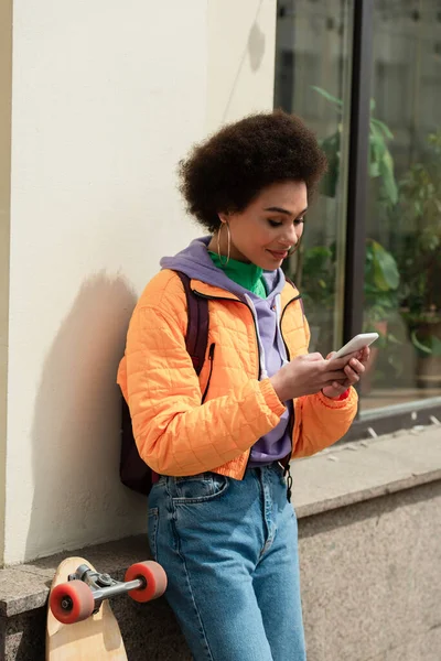 Mujer Afroamericana Sonriendo Mientras Usa Teléfono Inteligente Cerca Longboard Aire — Foto de Stock